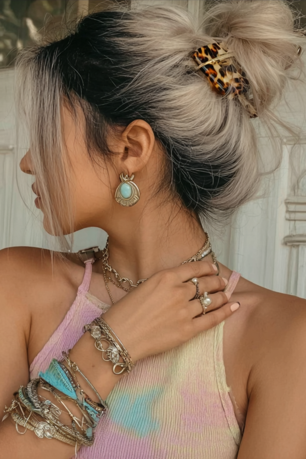 Side profile of a woman with platinum hair in a tortoiseshell clip, turquoise drop earring, and multiple bracelets against a light background.